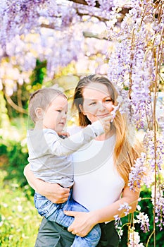 Mother is holding her 6-year old in her arms and showing him wysteria tree