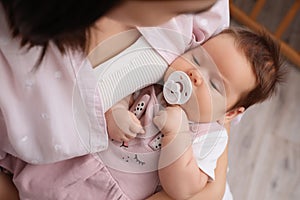 Mother holding her cute little baby with pacifier indoors, above view