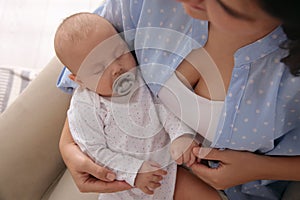 Mother holding her cute sleeping baby with pacifier on armchair, above view