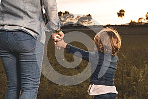 A mother holding her little daughter`s hand in the field