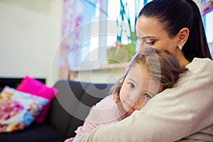 Mother holding her little sad daughter in her arms