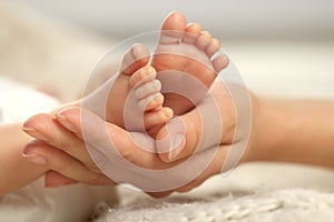 Mother holding her newborn baby, closeup view on feet. Lovely family