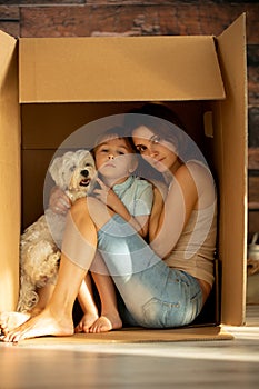 Mother, holding her toddler child in her arms, sitting in cardboard box
