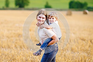 Mother holding kid boy on arms on wheat field in summer