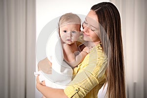 Mother holding cute little baby wrapped with towel indoors after bath