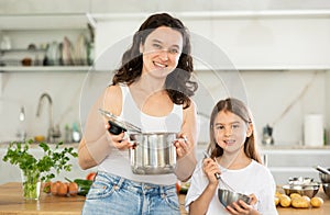 Mother holding saucepan and preteen daughter standing at table