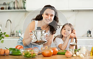 Mother holding saucepan and preteen daughter standing at table