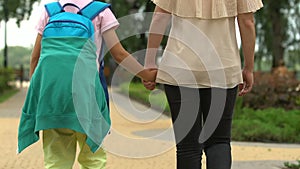 Mother holding son by hand, walking to school for first time, encouraging kid