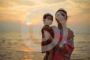 mother holding and talking toddler baby girl on sea beach at sunset