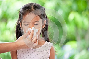 Mother holding tissue and help sick daughter wiping nose