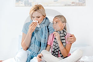 Mother holding tissue near ill kid with digital thermometer in mouth