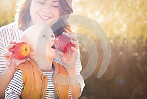 Mother holding two red ripe apples. Child (baby boy, kid) eating healthy food, snack.