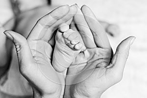 Mother holds the baby& x27;s foot in her hands. Close-up.Black and white photo.Concept of motherhood and children& x27;s day