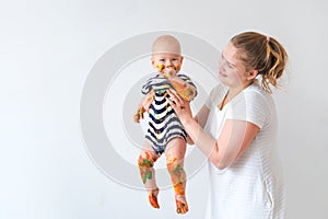 Mother holds cheerful grimy dirty baby playing with paint over white wall background. Happy leasure and fun crazy play