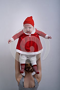 Mother holds a displeased baby in a Santa Claus costume over his head