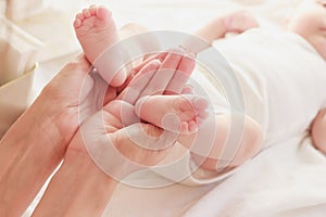Mother holds feet of her baby in the hands, indoors, blurred background