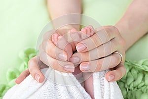 Mother holds the feet of the newborn baby with her hands, fingers on the foot, maternal care, love and family hugs, tenderness.