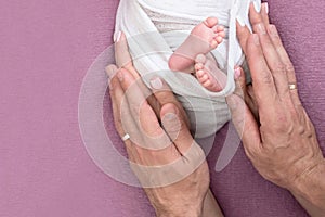 Mother holds the feet of the newborn baby with her hands, fingers on the foot, maternal care, love and family hugs, tenderness