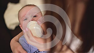 Mother holds four months old baby infant boy on her hands, feeding him milk from bottle