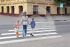 Mother holds hand of children and crossing road