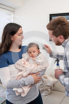 A mother holds her baby while the father is combing the baby& x27;s hair using a blue brush with soft white bristles.