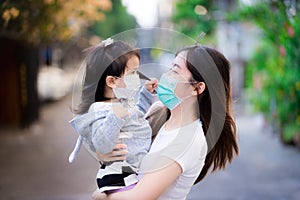 Mother holds her daughter. Mother and child wear a mask. Both looked at each other warmly.