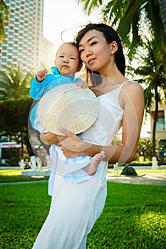 A mother holds her little daughter in traditional vietnam clothers aodai in her arms on the beach near palms