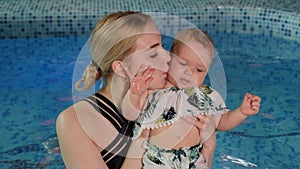 A mother holds her one-year-old daughter in her arms and kisses her in the pool.
