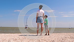 The mother holds her son`s hand, pointing to a boat in the distance. Happy family, two generations of travel. teamwork