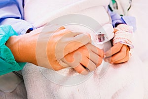 Mother holds her son`s hand to encourage her in a hospital bed before an operation