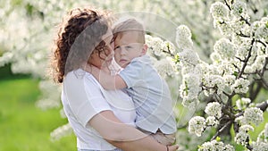 mother holds her young son in a flowering spring garden. parental love and care