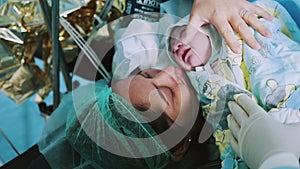 Mother Holds Newborn Baby in Hospital. Mother Holding Her Newborn Baby on Her Chest Just After Delivery. First Sight of