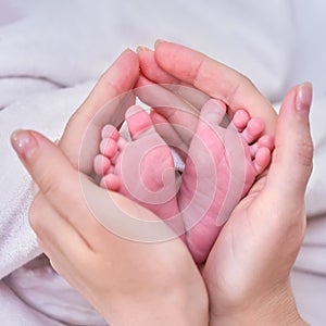 The mother holds the small child foot in her palms. Large female hands and feet of a newborn baby