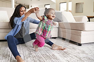 Mother At Home Encouraging Baby Daughter To Take First Steps