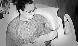 Mother in Hospital Bed Jusrt After Giving Birth Holds Newborn Baby Boy Wrapped in a Blanket as he Sleeps. Black & White Photo