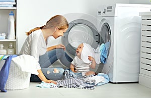 Mother a housewife with a baby fold clothes into the washing ma