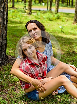 Mother hugging her little daughter resting on her sholder against of green grass in the forest photo