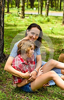 Mother hugging her little daughter resting on her sholder with closed eyes against of green grass in the forest photo