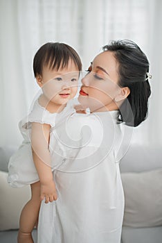 Mother hugging and kissing her little girl in living room, Kid at home