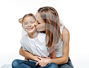 Mother hugging and kissing smiling daughter