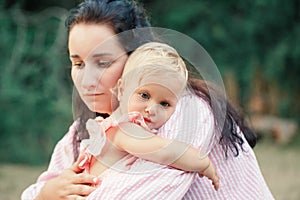 Mother hugging pacifying sad upset toddler girl. Family young mom and tired baby in park outdoor. Bonding attachment relationship