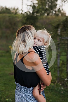 Mother hugs blonde daugher in striped dress in park