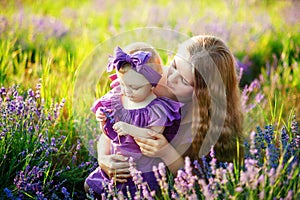 Mother hugs her little daughter in the rays of the setting sun, wearing long lilac dresses