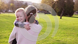 Mother hugs and whirls with her little son in park at sunset