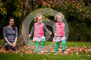 Mother and identical twins having fun in autumn in the park, blond cute curly girls, happy family, beautiful girls in pink jackets