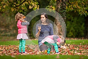 Mother and identical twins having fun in autumn in the park, blond cute curly girls, happy family, beautiful girls in pink jackets