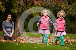 Mother and identical twins having fun in autumn in the park, blond cute curly girls, happy family, beautiful girls in pink jackets