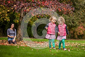 Mother and identical twins having fun in autumn in the park, blond cute curly girls, happy family, beautiful girls in pink jackets