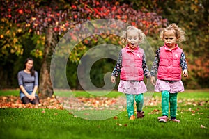 Mother and identical twins having fun in autumn in the park, blond cute curly girls, happy family, beautiful girls in pink jackets