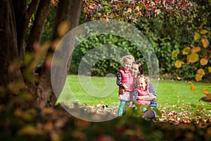 Mother and identical twins having fun in the park in autumn, blond cute curly girls, happy family, beautiful girls in pink jackets